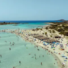 Piękna, słoneczna kreta pogoda w lipcu. Tłumy ludzi kąpią się w krystalicznie czystej wodzie i odpoczywają na piaszczystej plaży pod parasolami.