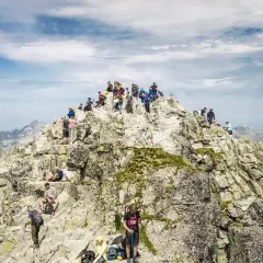 Grupa turystów na skalistym szczycie, podziwiająca panoramę. Nawet najtrudniejsze momenty wspinaczki wynagradza widok.