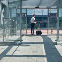 Pilot z walizką czeka przed wejściem do terminalu. Jak dolecieć na Azory? Kierunek Terminal D.