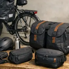 Rowerzysta wybiera, jakie sakwy rowerowe zabrać na wyprawę. Obok roweru leżą czarne torby, kask i bidon.