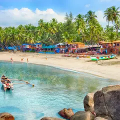 Goa kiedy jechać? Słoneczna plaża z palmami, kolorowe chatki i łodzie. Idealne miejsce na wakacje.