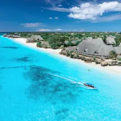 Idealna pogoda na Zanzibarze w październiku: turkusowa woda, biała plaża i łódź z turystami.