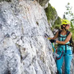 Kobieta w kasku i sprzęcie wspinaczkowym pokonuje via ferrata, czyli ubezpieczoną trasę w górach.