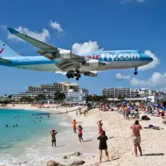 Samolot Airfly.com nisko przelatuje nad plażą pełną turystów. To słynne lotnisko przy plaży, gdzie można poczuć podmuchy odrzutowców.