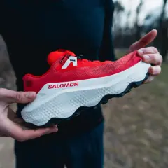 Czerwony but Salomon Ultra Glide 4 w rękach biegacza, gotowy na trailowe przygody.