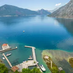 Widok na zatokę kotorską z górami w tle. Woda jest turkusowa, widać łodzie i małe plaże.