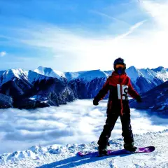 Snowboardzista w hardshellowej kurtce stoi na szczycie góry, nad morzem chmur.