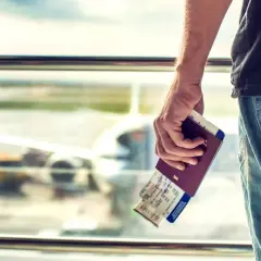 Ręka trzyma paszport i bilety lotnicze. W tle widać samolot, a podróżni martwią się o strajki na lotniskach.