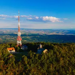 Wieża telekomunikacyjna na szczycie góry Ślęża, otoczona lasem, z widokiem na rozległą dolinę.