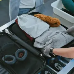 Kontrola bagażu rejestrowanego na lotnisku. Ręce w rękawiczkach układają ubrania w walizce.