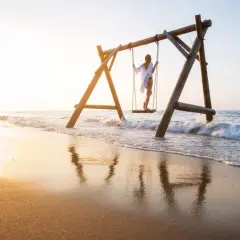 Dziewczyna na huśtawce na plaży w Turcji, fale obmywają piasek, złote światło zachodu słońca.