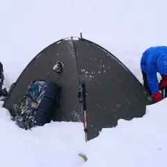 Zimowy biwak. Namiot w śniegu, plecaki i kijki w góry gotowe do akcji.