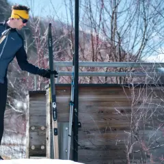 Mężczyzna w żółtej opasce i sportowym ubraniu na narty biegowe trzyma narty.