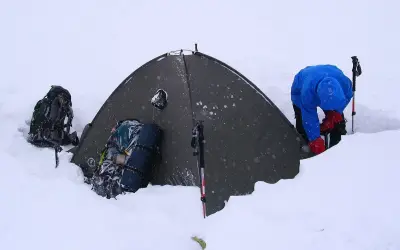 Zimowy biwak. Namiot w śniegu, plecaki i kijki w góry gotowe do akcji.