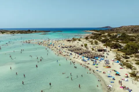 Piękna, słoneczna kreta pogoda w lipcu. Tłumy ludzi kąpią się w krystalicznie czystej wodzie i odpoczywają na piaszczystej plaży pod parasolami.