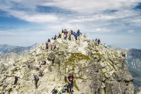 Grupa turystów na skalistym szczycie, podziwiająca panoramę. Nawet najtrudniejsze momenty wspinaczki wynagradza widok.