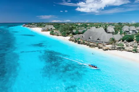 Idealna pogoda na Zanzibarze w październiku: turkusowa woda, biała plaża i łódź z turystami.