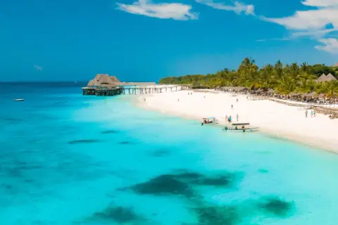 Zanzibar w lutym: słoneczna plaża, turkusowa woda, palmy i drewniany pomost. Idealna pogoda na wakacje.