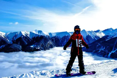 Snowboardzista w hardshellowej kurtce stoi na szczycie góry, nad morzem chmur.