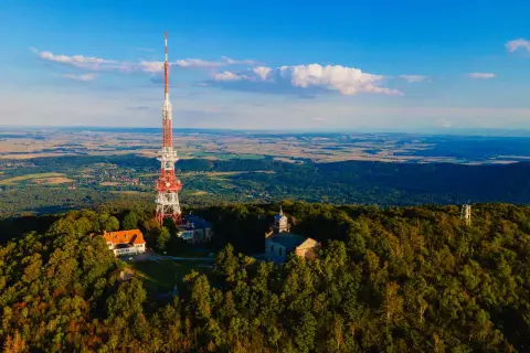 Wieża telekomunikacyjna na szczycie góry Ślęża, otoczona lasem, z widokiem na rozległą dolinę.