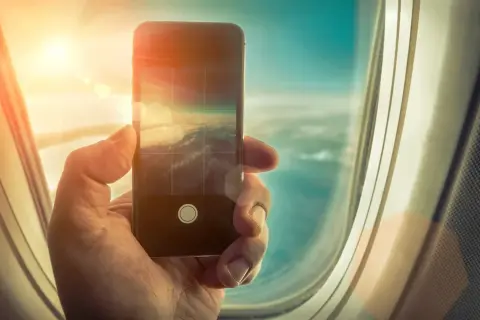 Dłoń trzyma smartfon, robiąc zdjęcie chmur z samolotu. Czy w samolocie można korzystać z telefonu? Tak, do robienia zdjęć!