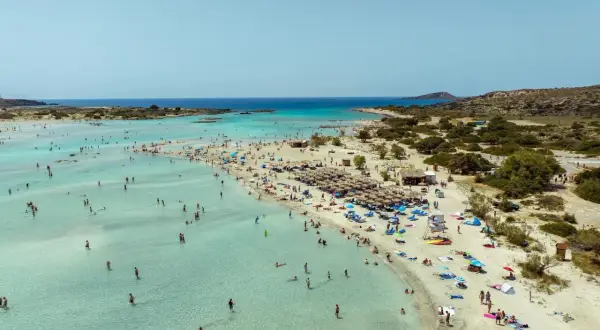 Piękna, słoneczna kreta pogoda w lipcu. Tłumy ludzi kąpią się w krystalicznie czystej wodzie i odpoczywają na piaszczystej plaży pod parasolami.