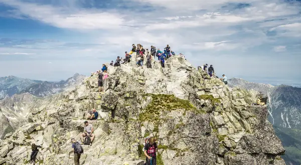 Grupa turystów na skalistym szczycie, podziwiająca panoramę. Nawet najtrudniejsze momenty wspinaczki wynagradza widok.