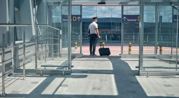 Pilot z walizką czeka przed wejściem do terminalu. Jak dolecieć na Azory? Kierunek Terminal D.