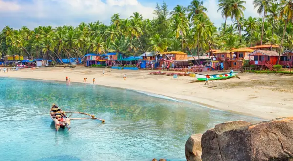 Goa kiedy jechać? Słoneczna plaża z palmami, kolorowe chatki i łodzie. Idealne miejsce na wakacje.