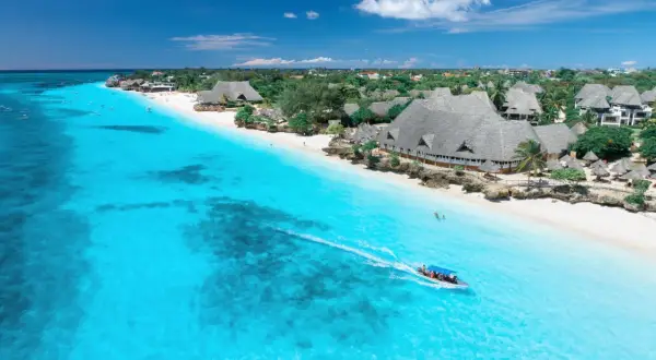 Idealna pogoda na Zanzibarze w październiku: turkusowa woda, biała plaża i łódź z turystami.