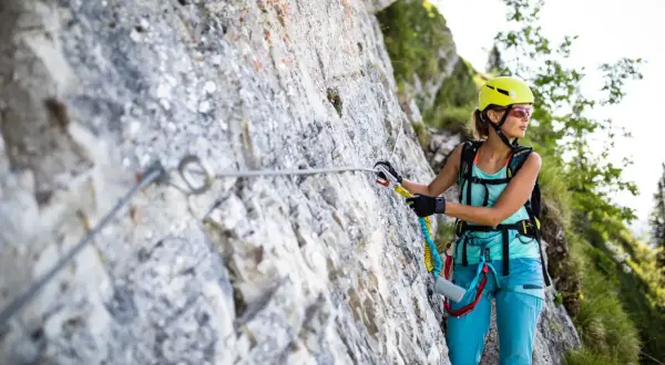 Kobieta w kasku i sprzęcie wspinaczkowym pokonuje via ferrata, czyli ubezpieczoną trasę w górach.