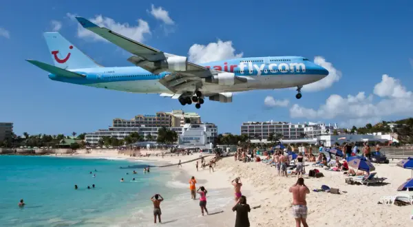 Samolot Airfly.com nisko przelatuje nad plażą pełną turystów. To słynne lotnisko przy plaży, gdzie można poczuć podmuchy odrzutowców.