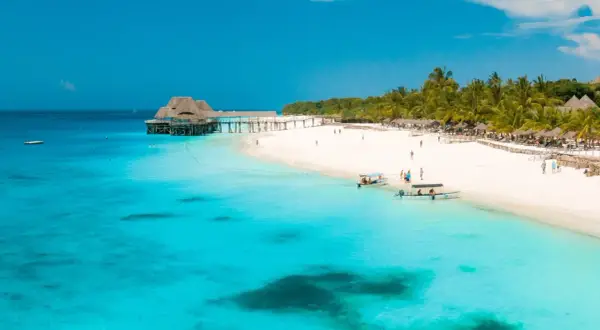 Zanzibar w lutym: słoneczna plaża, turkusowa woda, palmy i drewniany pomost. Idealna pogoda na wakacje.