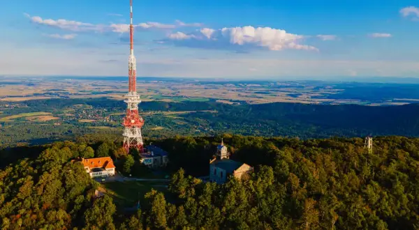 Wieża telekomunikacyjna na szczycie góry Ślęża, otoczona lasem, z widokiem na rozległą dolinę.