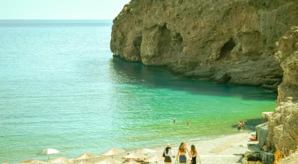 Kreta, sierpień: trzy dziewczyny idą na plażę z turkusową wodą i skalistymi klifami. Idealna pogoda na wakacje.