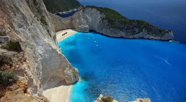 Widok na Zatokę Wraku na Zakynthos, Grecja. Wrak statku leży na piaszczystej plaży otoczonej białymi klifami i turkusowym morzem.