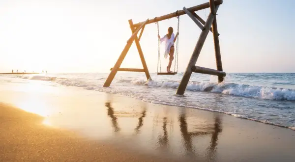 Dziewczyna na huśtawce na plaży w Turcji, fale obmywają piasek, złote światło zachodu słońca.
