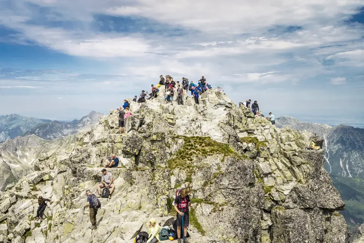Grupa turystów na skalistym szczycie, podziwiająca panoramę. Nawet najtrudniejsze momenty wspinaczki wynagradza widok.