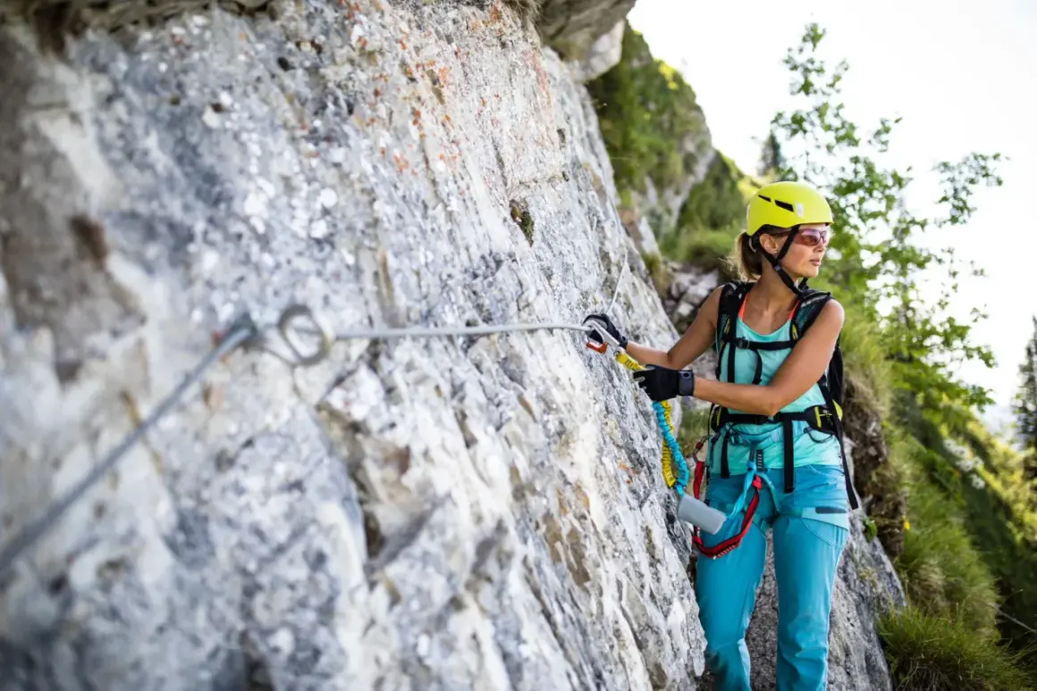 Kobieta w kasku i sprzęcie wspinaczkowym pokonuje via ferrata, czyli ubezpieczoną trasę w górach.