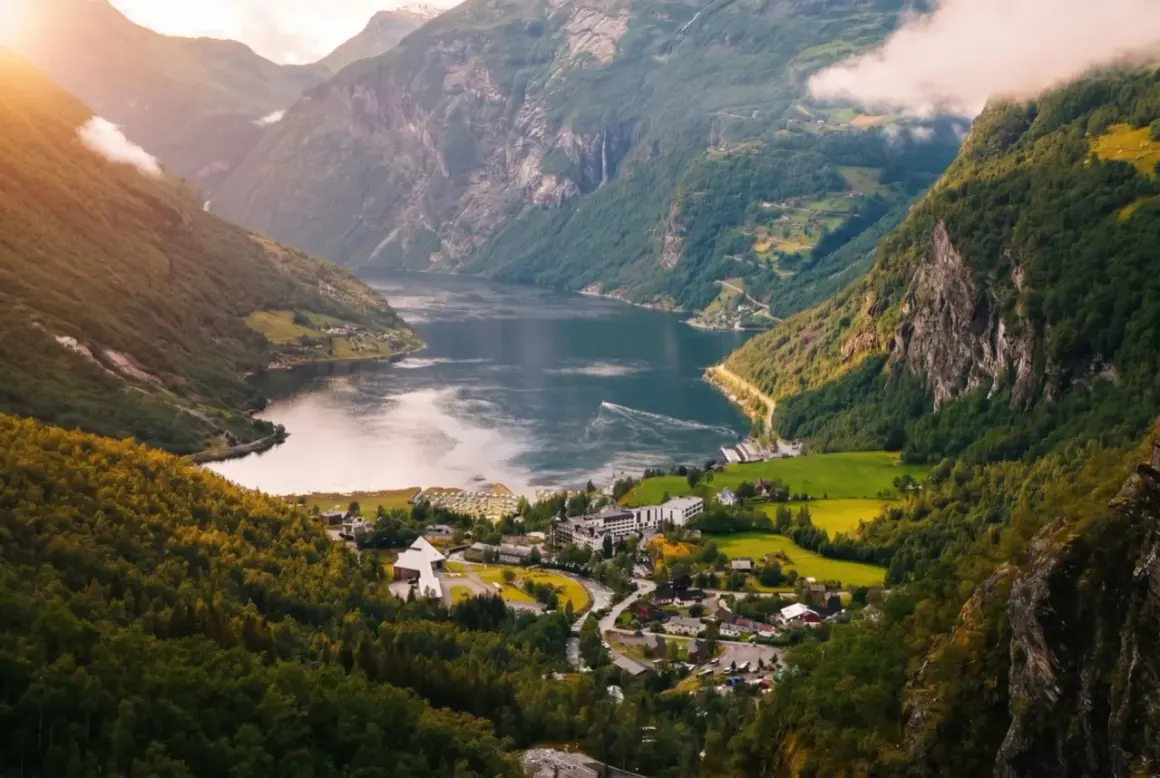 Malowniczy widok na fiord w Norwegii. Pogoda w lipcu sprzyja zwiedzaniu, słońce oświetla zielone zbocza i spokojną taflę wody.