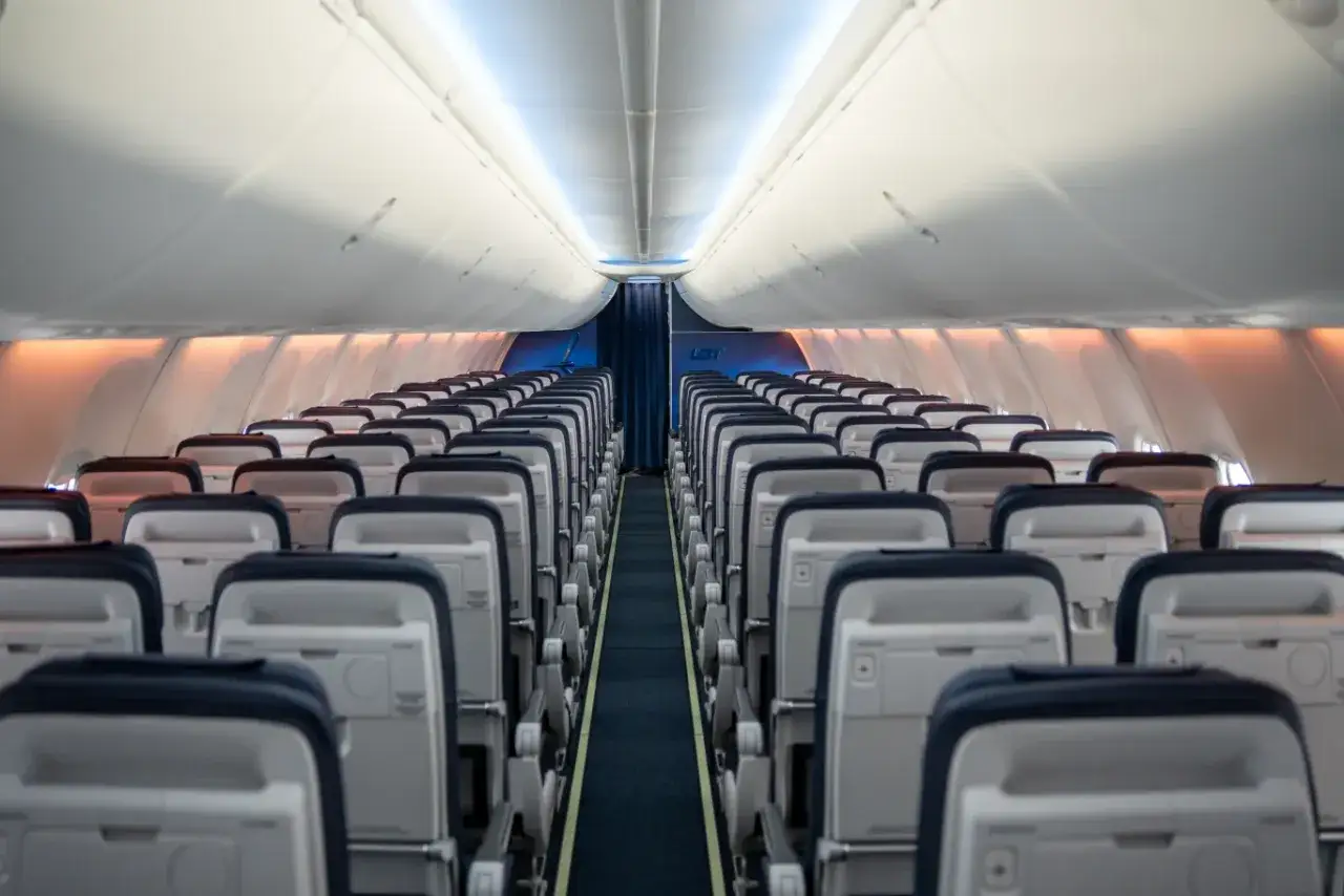 Puste rzędy siedzeń w samolocie Boeing 737. Widok na korytarz i liczne miejsca pasażerskie.