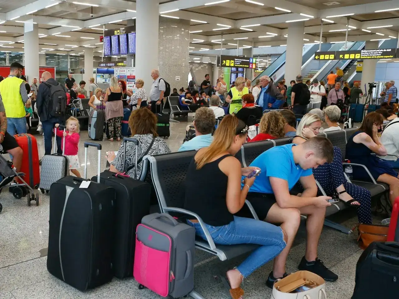 Ludzie z bagażami czekają na lotnisku, być może z powodu strajków na lotniskach.