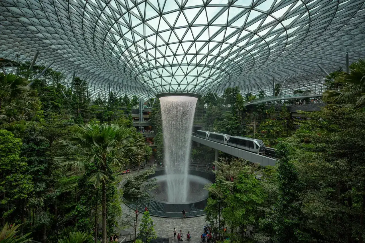 Wodospad HSBC Rain Vortex w porcie lotniczym Singapur-Changi, otoczony bujną zielenią i nowoczesnym pociągiem.