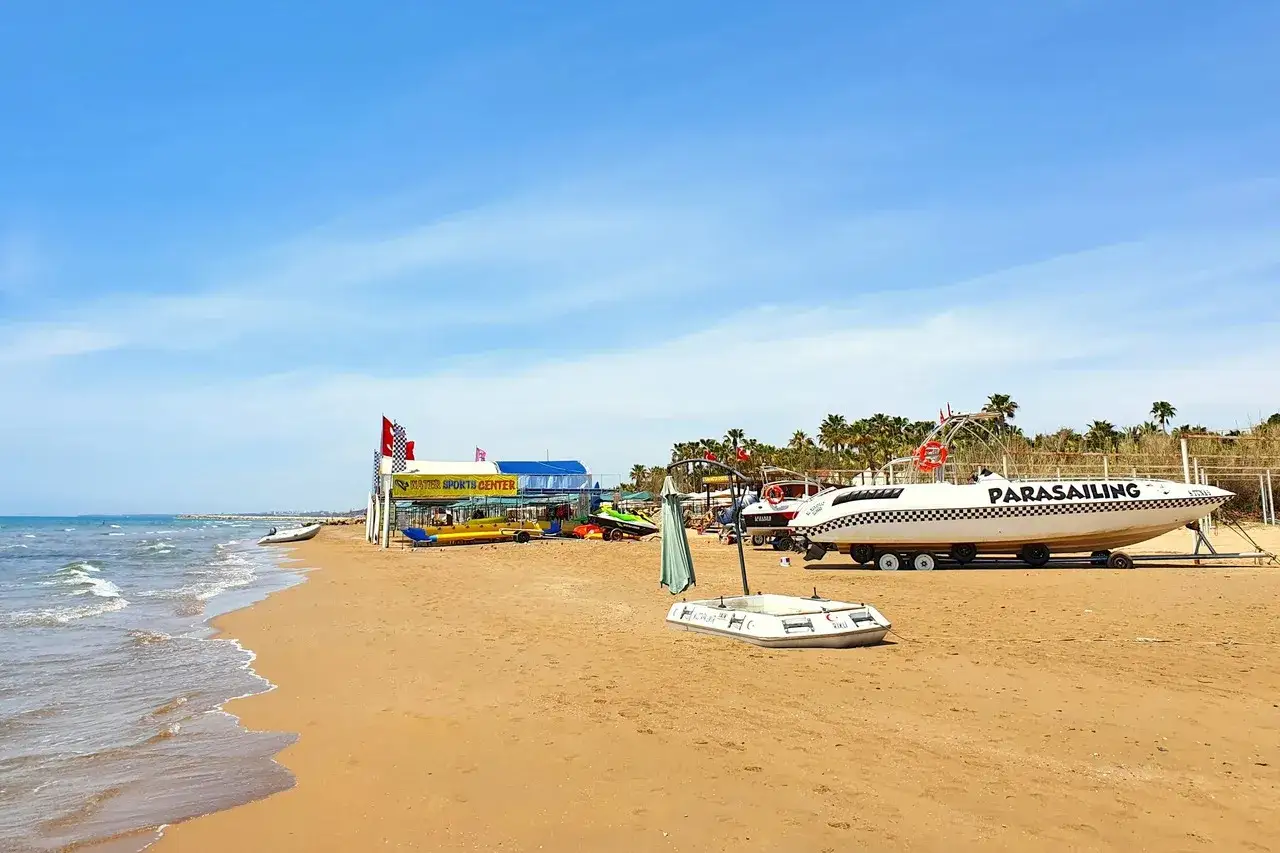 Słoneczna plaża w Side, Turcja, z łodziami do parasailingu i centrum sport&oacute;w wodnych.