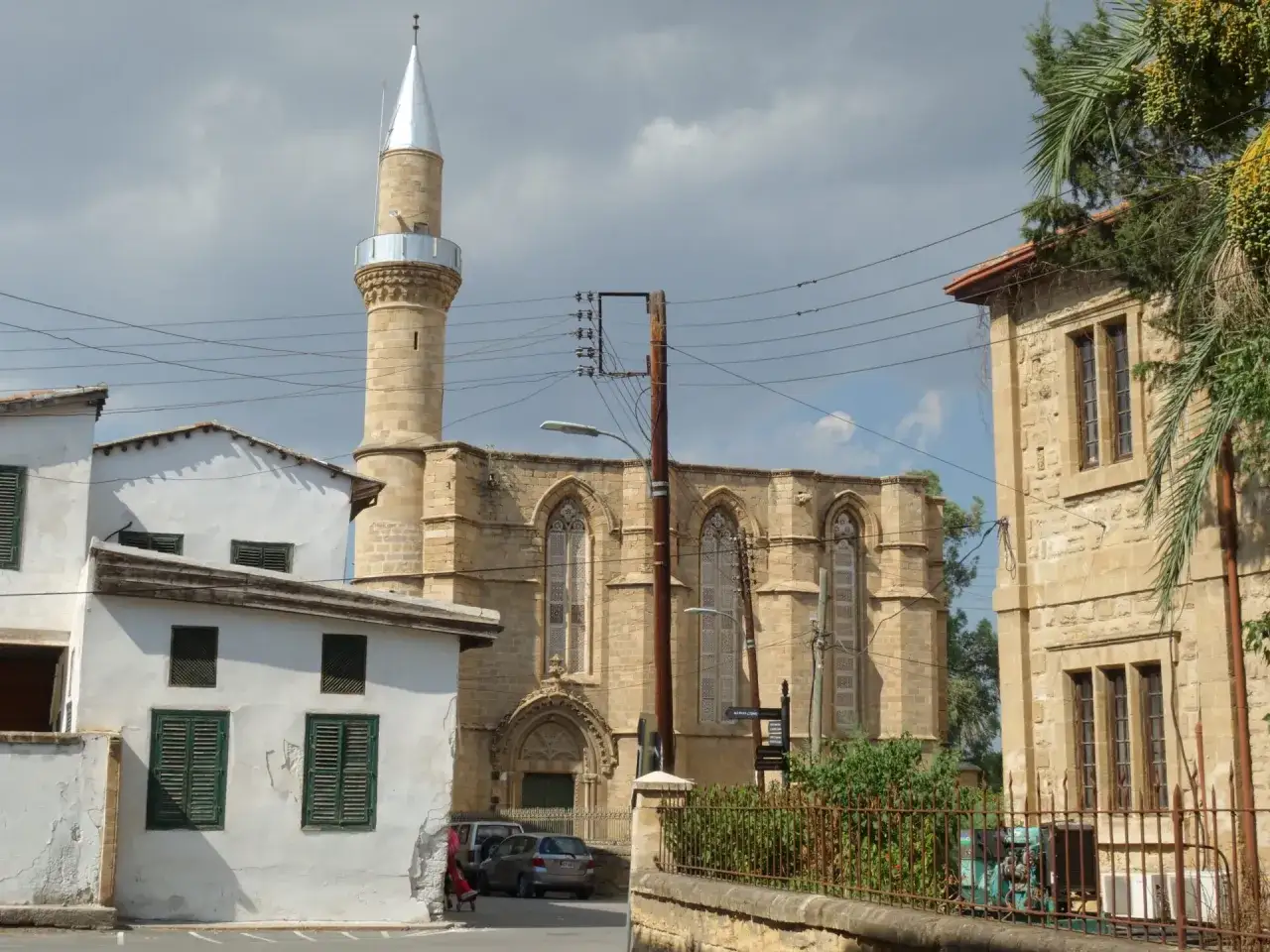 Nikozja co zobaczyć: minaret i zabytkowa budowla z kamienia, otoczone białymi domami i zielenią.