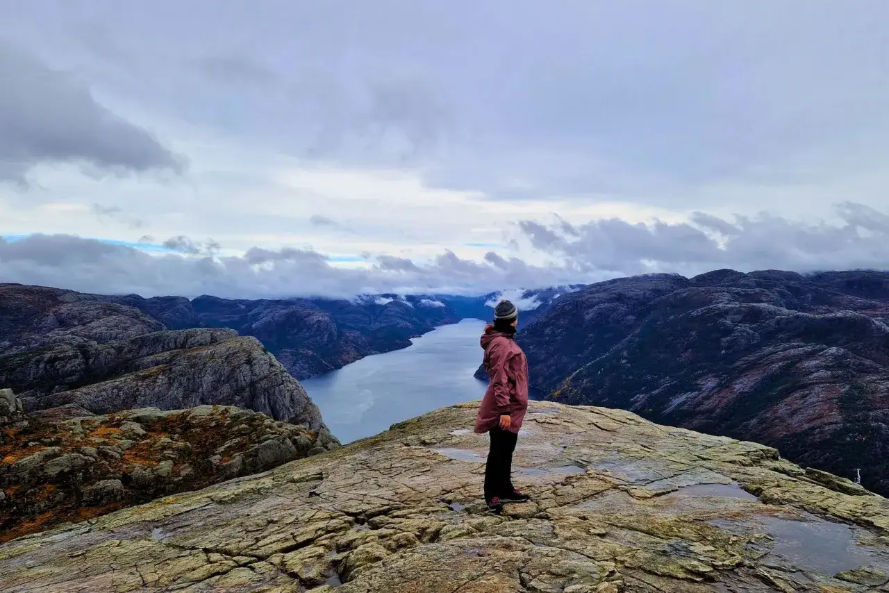 Widok na fiord z punktu widokowego. Osoba w kurtce podziwia krajobraz. To jedno z miejsc, które warto zobaczyć w okolicach Stavanger.