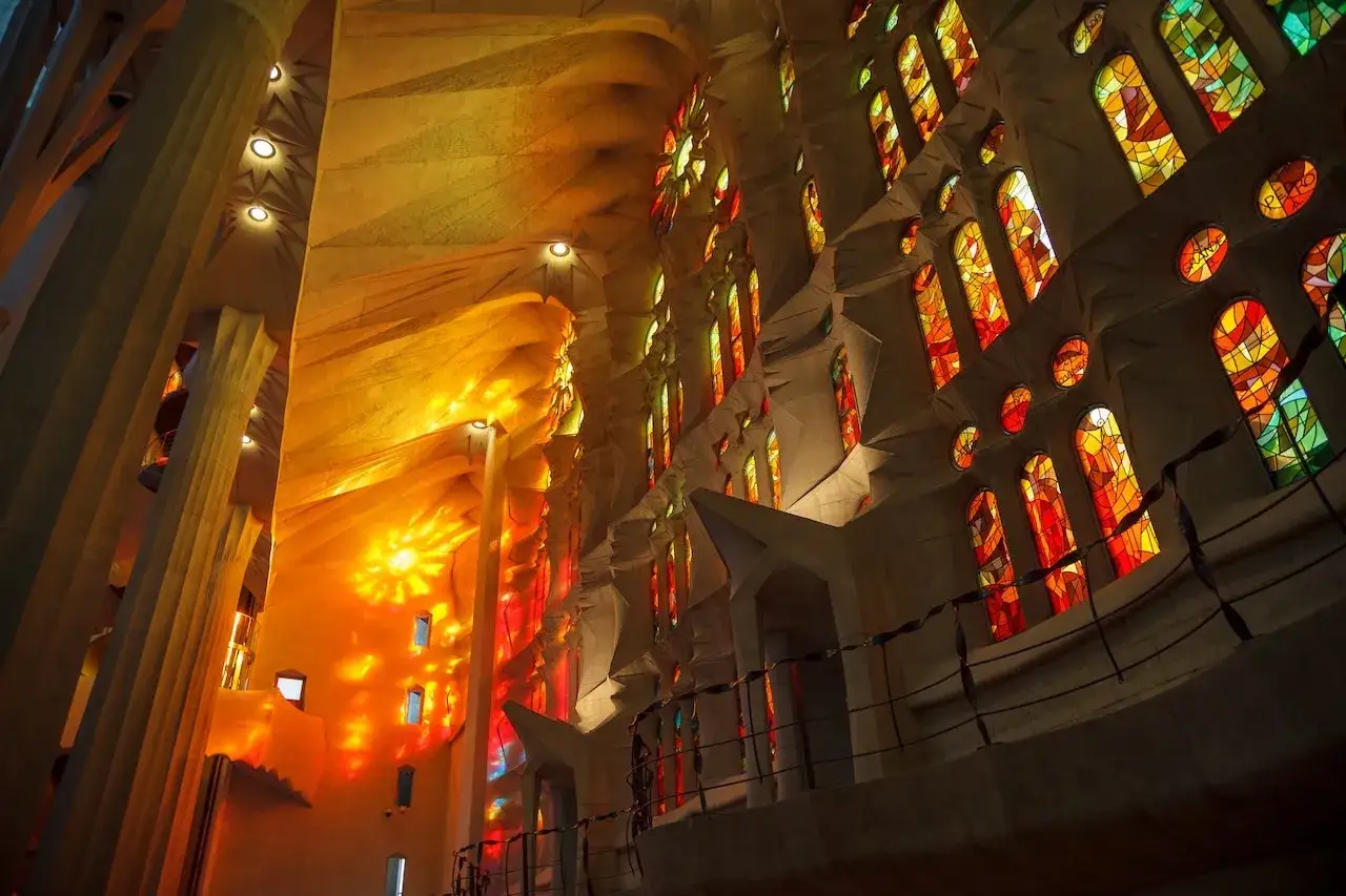 Wnętrze Sagrada Familia, gdzie światło prześwituje przez witraże, tworząc barwne refleksy. Dzieło architekta Gaudiego.