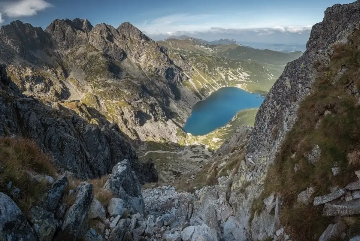 Widok z orla perc szlak na Morskie Oko. Kamienista ścieżka prowadzi w d&oacute;ł, a jezioro lśni w dole.