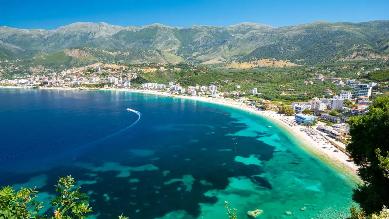 Słoneczna Albania w sierpniu: turkusowe morze, biała plaża i góry w tle. Idealna pogoda na wakacje.