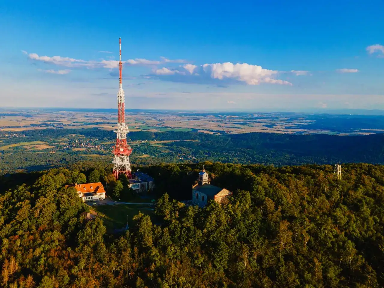Wieża telekomunikacyjna na szczycie g&oacute;ry Ślęża, otoczona lasem, z widokiem na rozległą dolinę.